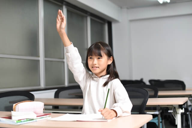 女の子が教室の中で挙手をしている画像
