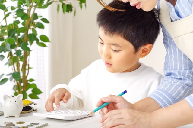 母親が男の子に電卓で計算する方法を教えている画像