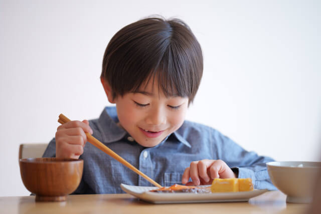 男の子が箸を使って焼き魚を食べようとしている画像