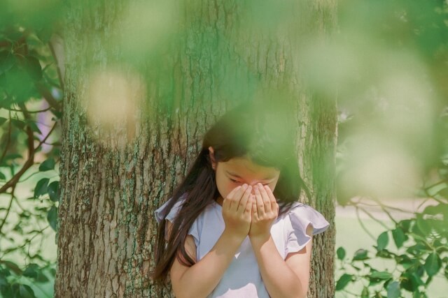 木の下で女の子が手で顔を隠している画像