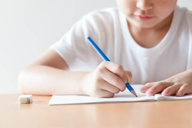 子供が鉛筆とノートを使って勉強している画像