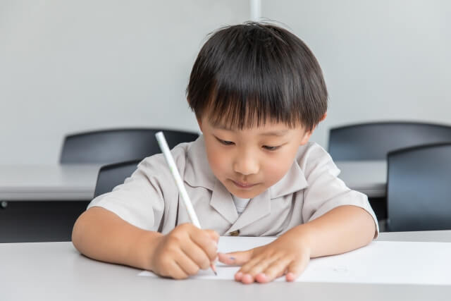 男の子が鉛筆でノートに書きこんでいる画像