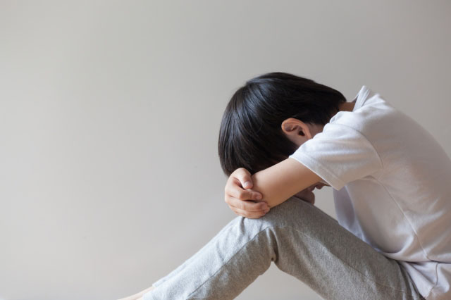 膝を抱えて顔をうずめる男の子の写真