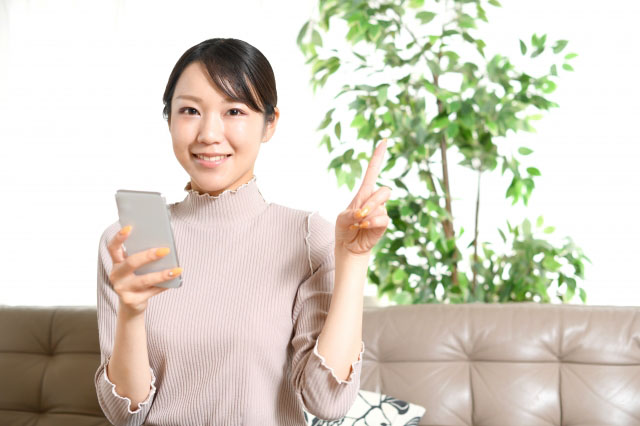 スマートフォン(スマホ)を片手に持ち、人差し指を立てる女性の写真