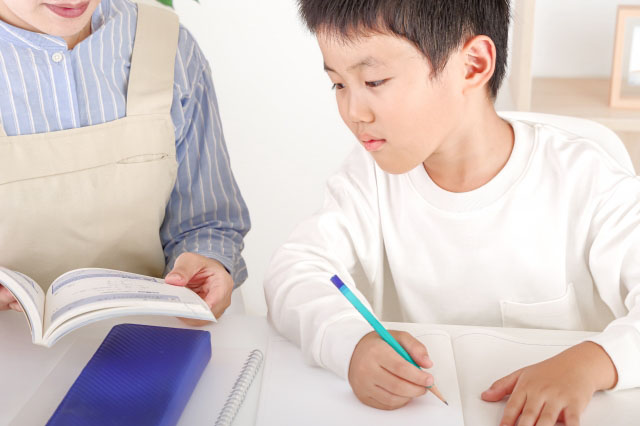教材を見る母親とノートを取ろうとする男の子の写真
