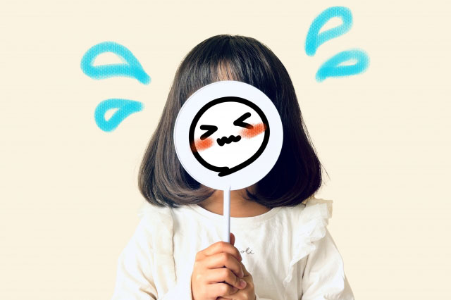 照れてる顔のイラストを自分の顔の前に持ってきている女の子の写真