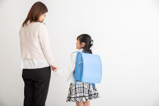 水色のランドセルを背負った女の子と手をつなぐ母親の写真