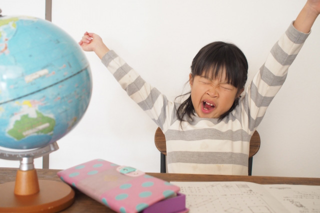 テキストの開かれた机に向かって欠伸をする子供の画像