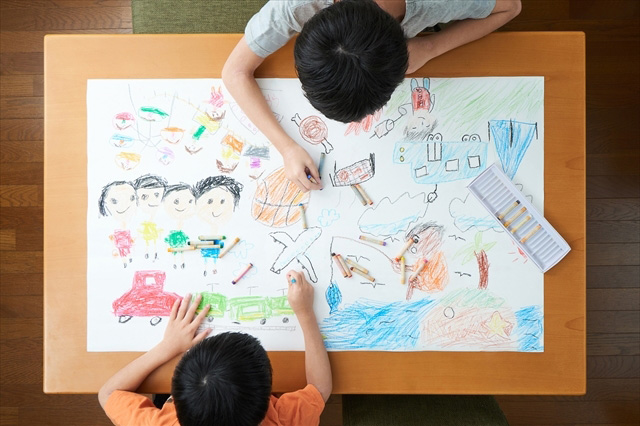 一枚の大きな画用紙に二人で絵を描くこどもの画像