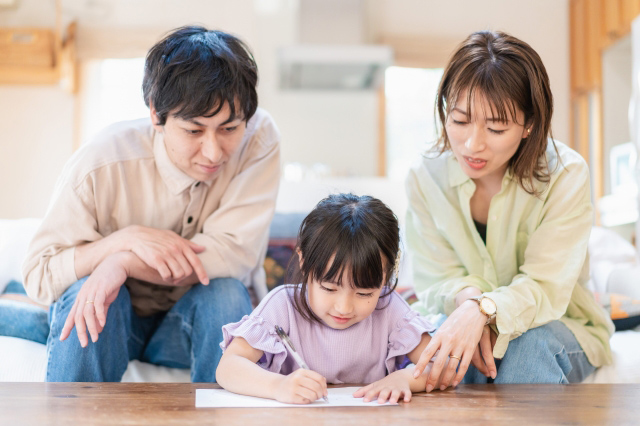 子供が勉強している様子を両親が見守っている画像