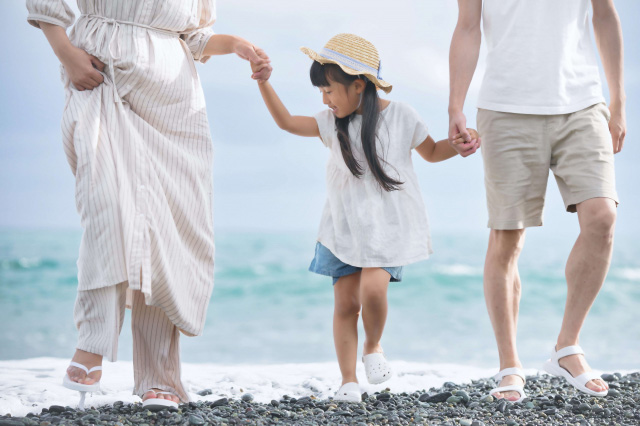 浜辺で両親と手をつないで迫ってくる波を見る子供の画像
