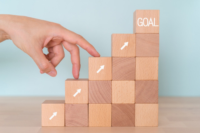 一番上に『GOAL』と書かれた階段のように積み重なった四角いブロックを、二本の指(人差し指と中指)が歩くように上っている画像