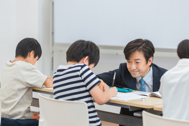 勉強している子供の教材に指をさして教えている先生の画像