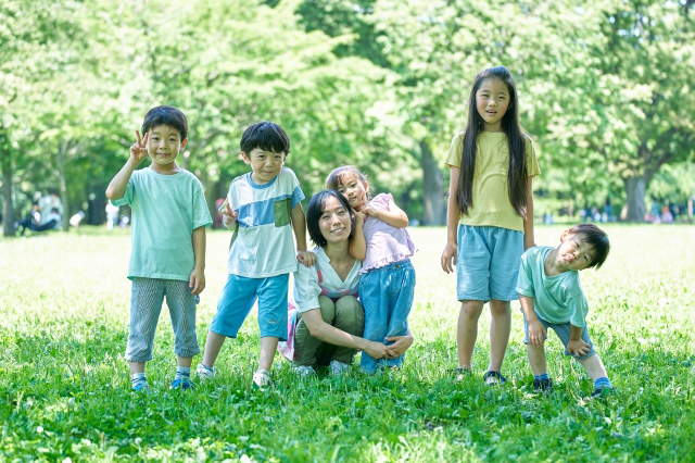 公園で子供たちと親が横一列に並んでピースサインをしている画像
