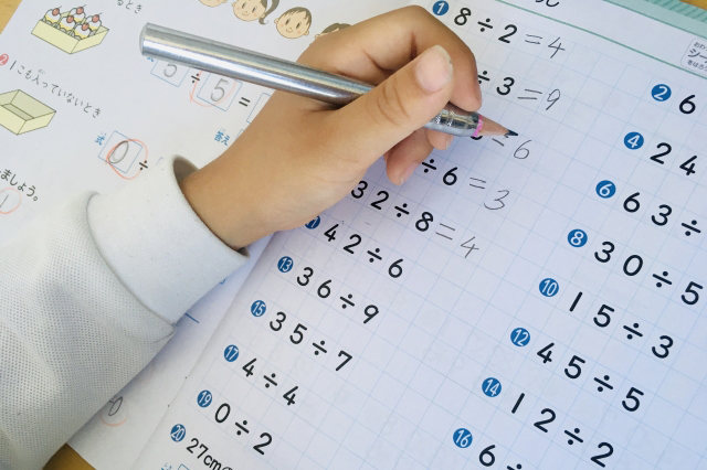 割り算の教材の問題を解く子供の手の画像