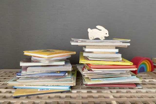 たくさんの絵本が積み上がりその上にウサギのおもちゃが乗っている画像