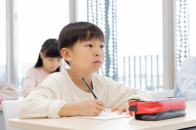 授業を受けながらノートに何かを書こうとしている子供の画像