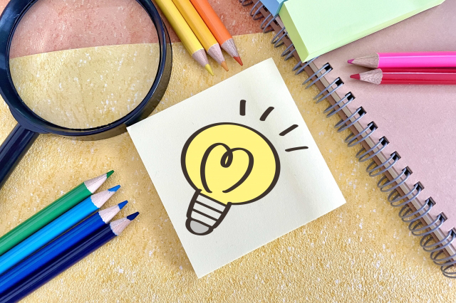 中央にひらめきマークのイラストがあり、周りに色鉛筆や虫眼鏡、ノートが置かれている画像
