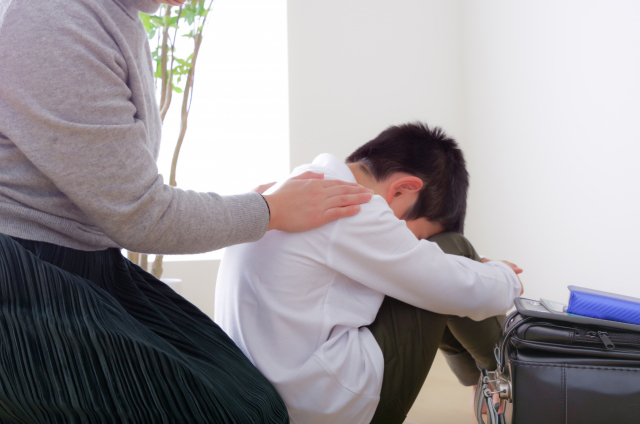 落ち込んでいる子供の背中にそっと手を置く母親の画像