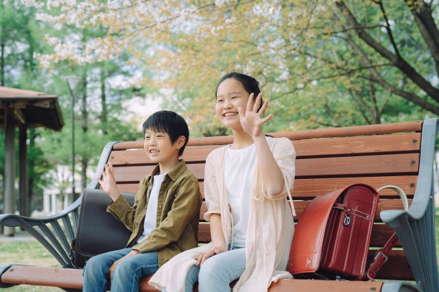 公園のベンチに座り手を振る子供たちの画像