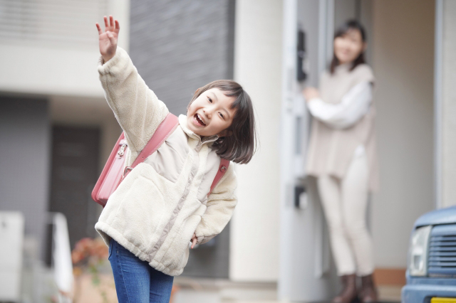 ランドセルを背負った子供が手を上げ挨拶している画像