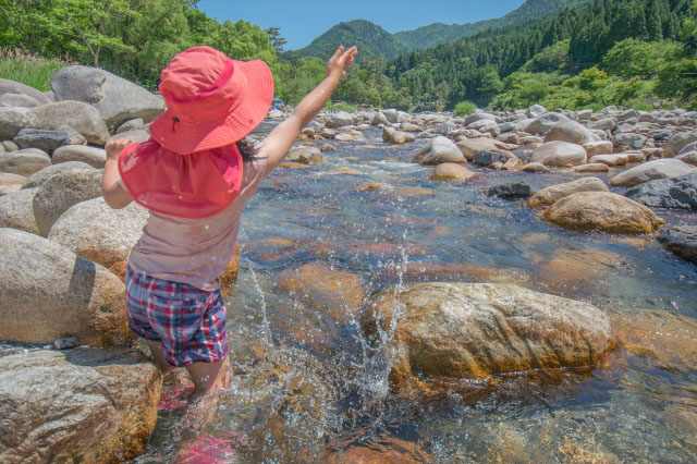 上流の川で水を飛ばす子供の写真
