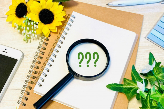 中央にノートが置いてありその上に「???」を映した虫眼鏡、周りに向日葵、スマートフォン、植物、付箋が置かれた画像