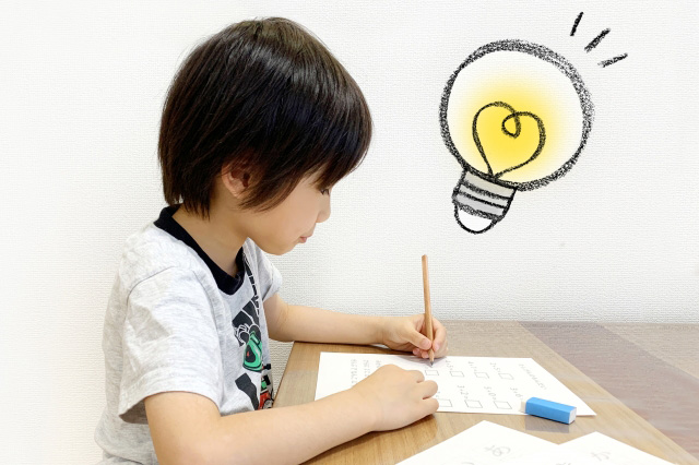 机に向かって勉強する子供の頭上に豆電球のイラストが描かれている画像