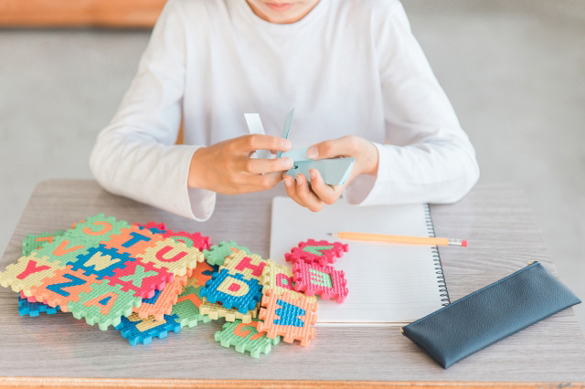 英字のパズルが置かれている机の上で単語帳を見ている子供の画像
