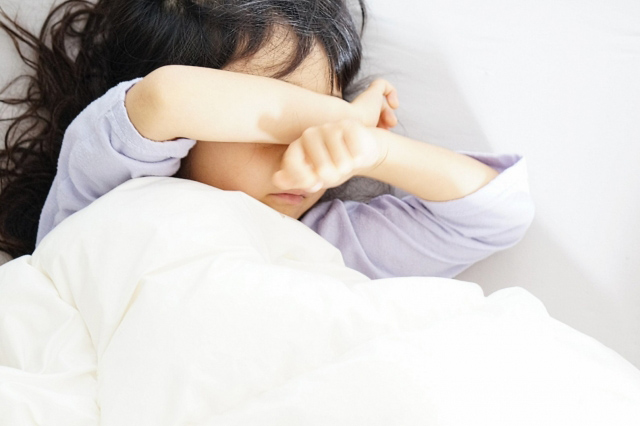 布団の中で眩しそうにする子供の画像