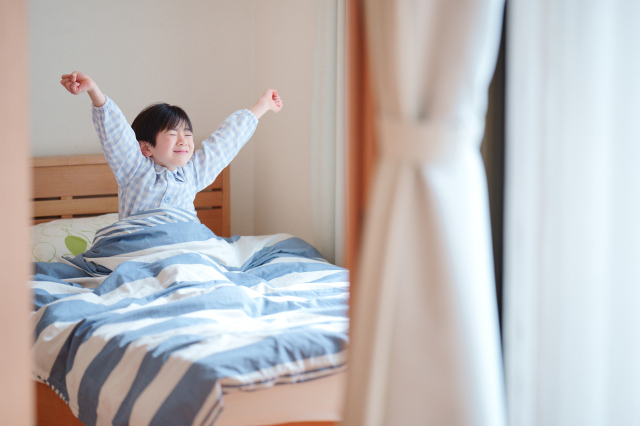 布団で伸びをする子供の画像