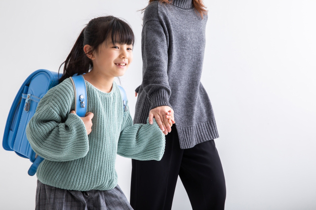 ランドセルを背負った子供が親と手をつないで歩いている画像