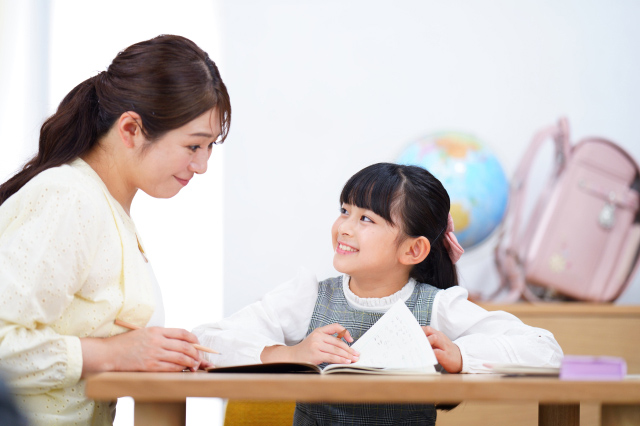 子供が勉強しているときに母親と目を合わせて微笑んでいる画像
