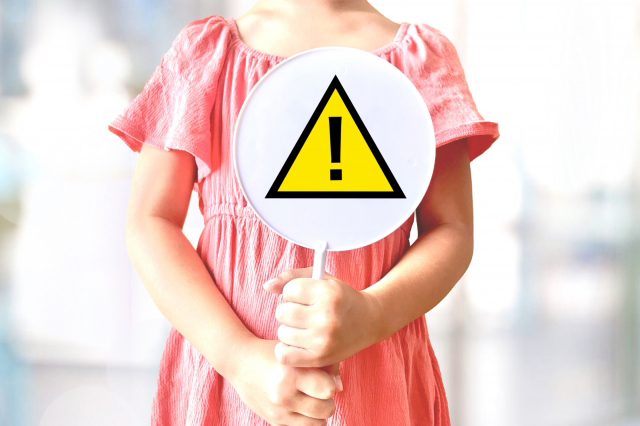 注意表記の看板を持った子供の画像